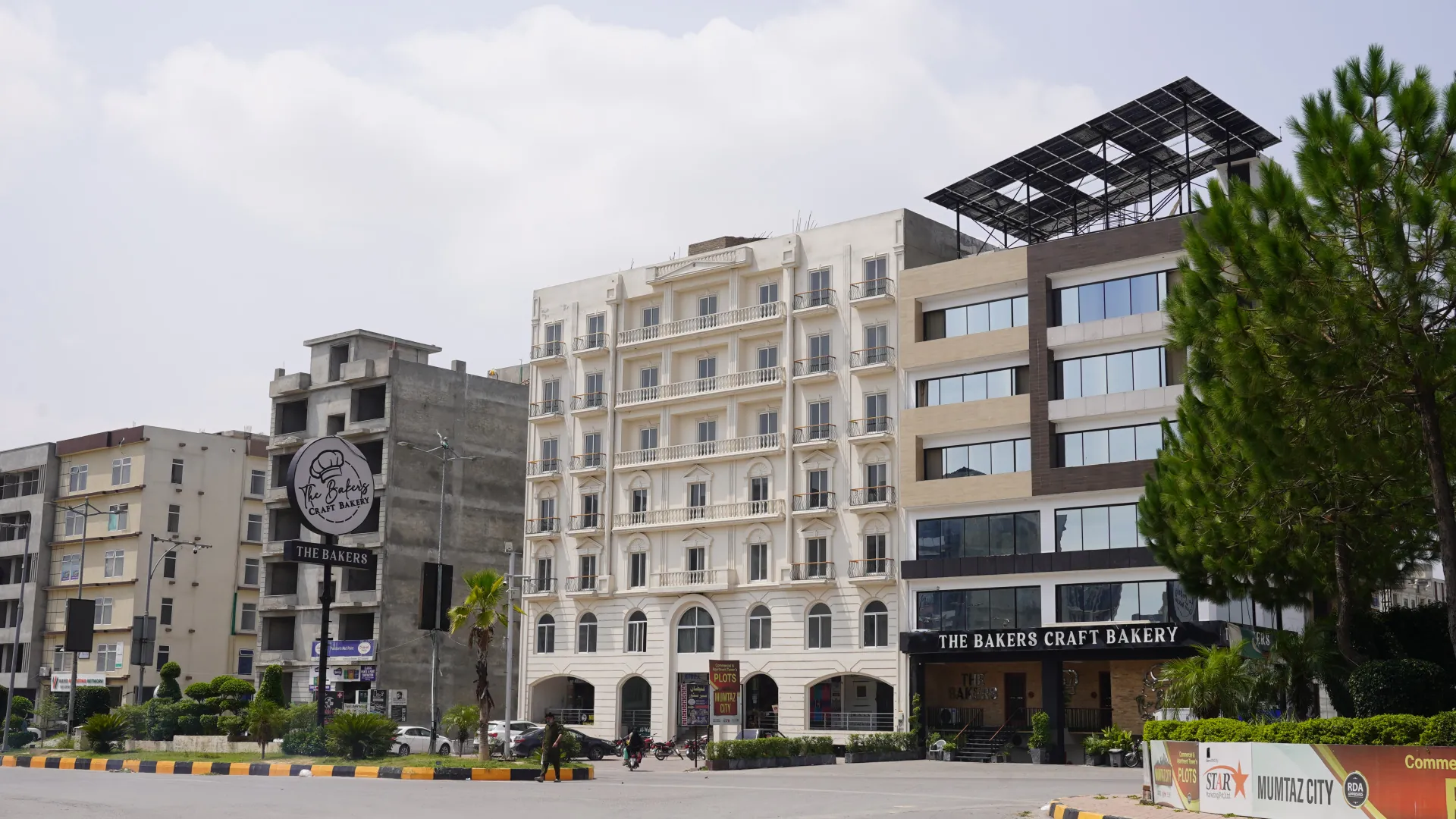 Commercial buildings and a bakery on the boulevard, beside a Mumtaz City sign