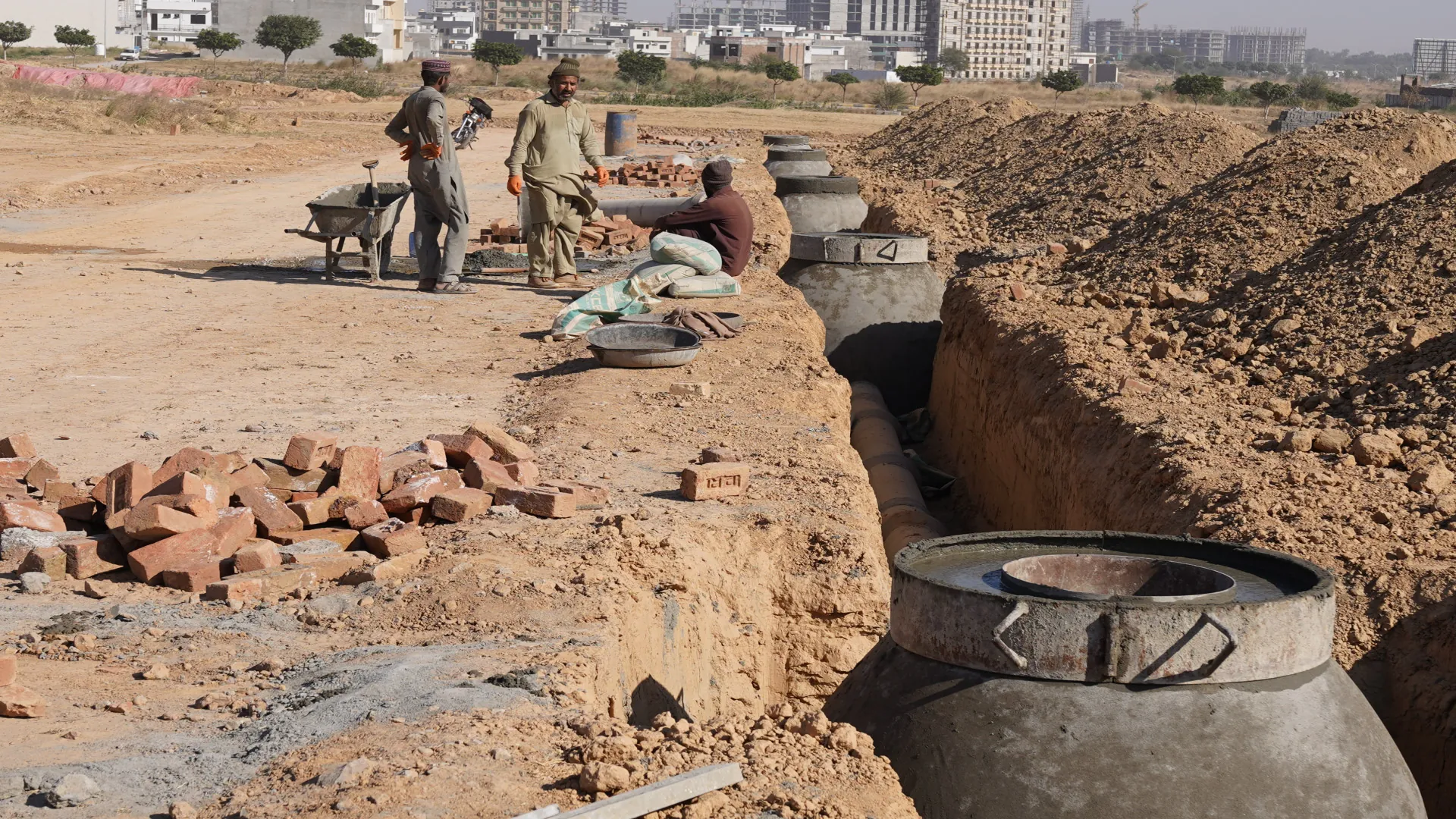 Workers laying sewer pipes and manholes in a trench