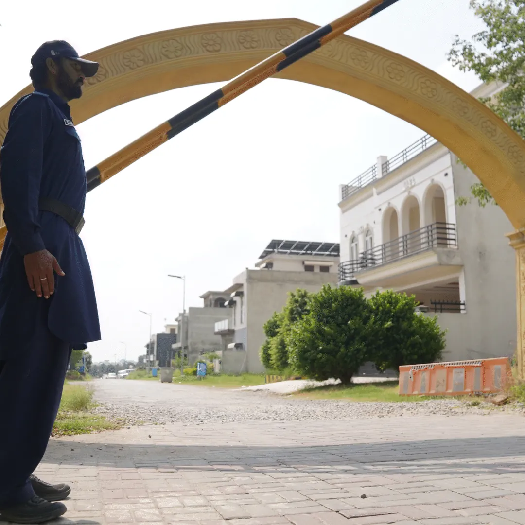 A security guard beside a raised barrier at an arched gate