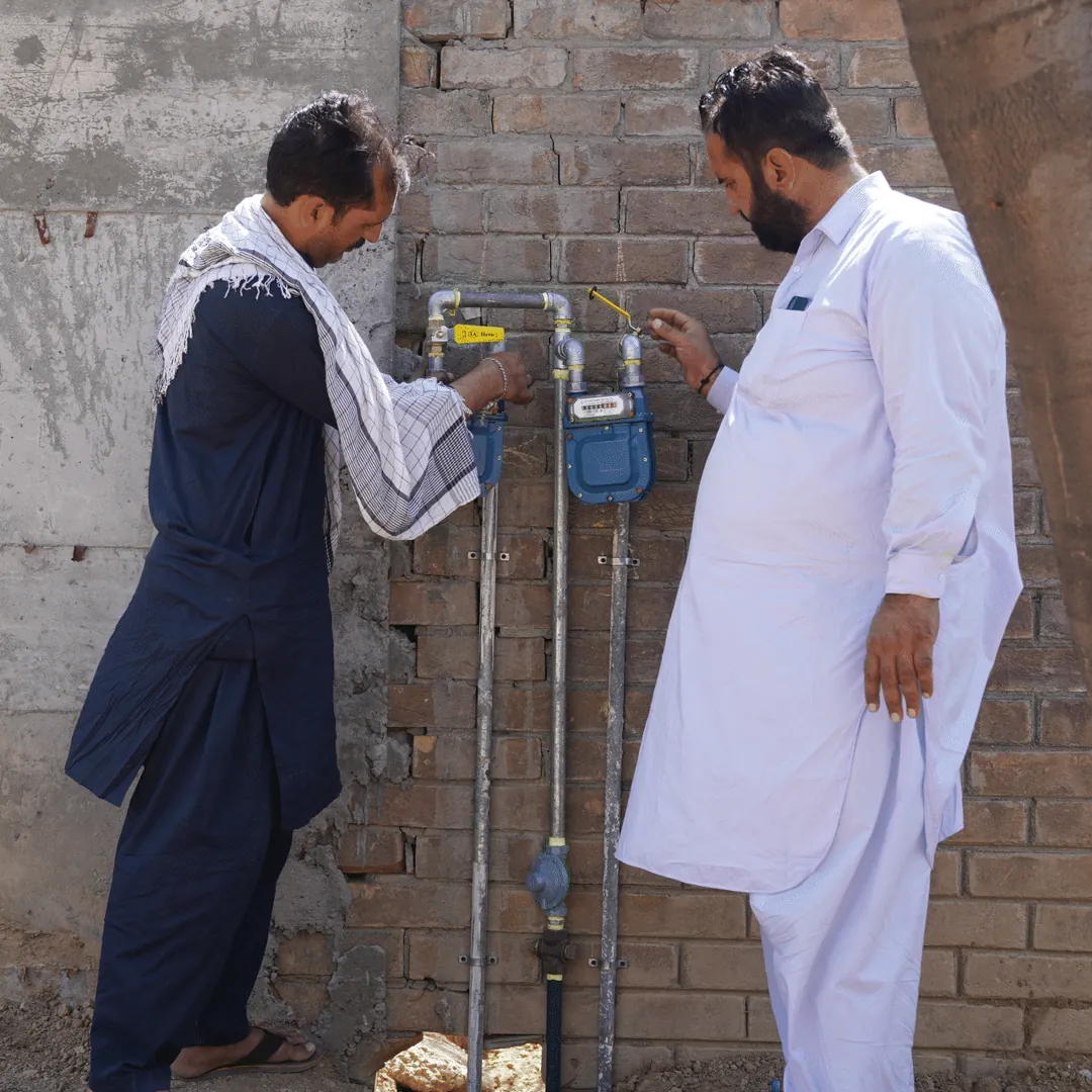 Two men beside gas meters on a wall
